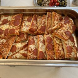 Rechteckige Pizzascheiben mit Salami liegen einladend in einem großen Tablett für ein Buffet bereit.