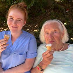 Zwei Frauen sitzen auf einer Parkbank und genießen ein Eis an einem sonnigen Tag.