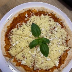 Eine frisch gebackene Pizza, in Stücke geschnitten und mit Basilikum garniert, liegt auf einem weißen Teller.