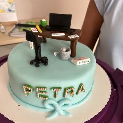 Eine Torte zeigt einen Miniatur-Schreibtisch mit Laptop und Stuhl, verziert mit dem Namen "Petra" in bunten Perlen.