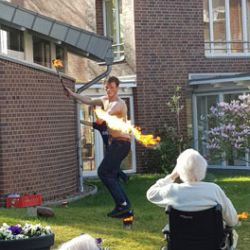 Ein Feuerschlucker zeigt im Garten eines Backsteingebäudes vor faszinierten Zuschauern eine beeindruckende Show.