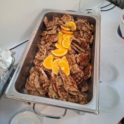 Gegrilltes Fleisch wird in einem Behälter serviert, dekoriert mit frischen Orangenscheiben.