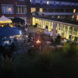 Menschen genießen ein abendliches Beisammensein im Innenhof mit Lagerfeuer und Lichtern unter einem beleuchteten Pavillon.