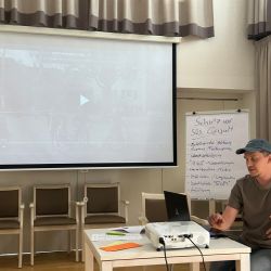 Ein Referent präsentiert ein Video zu Schutz vor sexueller Gewalt in einem Seminarraum mit Flipchart.