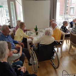 Ältere Menschen sitzen fröhlich in einem hellen Raum um einen Tisch und genießen Getränke und Gespräche.