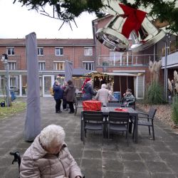 Senioren genießen eine weihnachtliche Party im Freien, während eine ältere Dame im Rollstuhl genüsslich Waffeln isst.