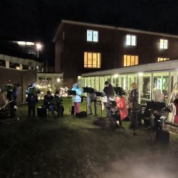 Eine Gruppe von Musikern spielt abends festliche Musik vor einem beleuchteten Gebäude im Freien.