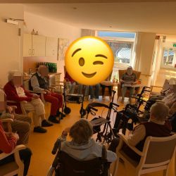 Ältere Menschen sitzen im Kreis in einem Gemeinschaftsraum und genießen die Gesellschaft, während Rollatoren bereitstehen.