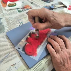 Hände gestalten kunstvoll mit Pinsel einen Schriftzug auf blauem Papier während einer kreativen Aktivität.
