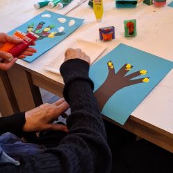 Eine Person kreiert lebendige Kunstwerke mit Farben und Stempeln auf blauen Papieren in einer kreativen Umgebung.