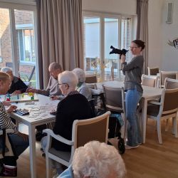 Eine Gruppe von Menschen spielt Spiele an einem Tisch, während eine Frau mit einer Kamera dokumentiert.