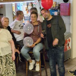 Eine Gruppe von Freunden feiert in einer Bar mit Ballons und Getränken, während sie fröhlich posieren.