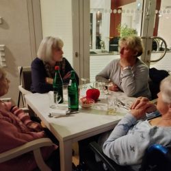 Vier ältere Frauen unterhalten sich lebhaft bei Getränken an einem Tisch in einem gemütlichen Café.