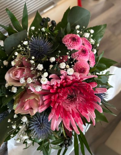 Ein bunter Blumenstrauß mit rosa Rosen, pinken und blauen Blüten sowie grünen Blättern.