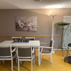 Ein gemütlicher Essbereich mit weißem Tisch und Stühlen, dekoriert mit Pflanzen und einem blumigen Wandbild.