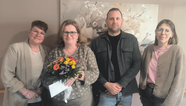Eine Gruppe von vier Personen feiert ein Jubiläum und hält einen Blumenstrauß als Zeichen der Wertschätzung.