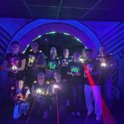 Eine Gruppe von Personen mit Lasergeschossen im Dunkeln, umgeben von buntem Licht, bereit für ein spannendes Spiel.