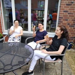 Drei Frauen sitzen entspannt auf einer sonnigen Terrasse und genießen gemeinsam Eiscreme.