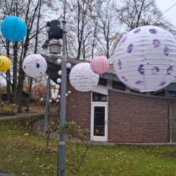 Bunte Laternen hängen dekorativ im herbstlichen Garten vor einem Backsteingebäude, inspiriert von einem Novembertag.