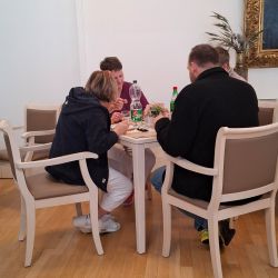 Vier Personen sitzen an einem Tisch in einem hellen Raum und diskutieren bei Getränken und Snacks.