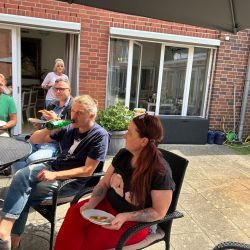 Eine Gruppe von Menschen sitzt gemütlich vor einem Backsteingebäude und genießt gemeinsam Essen und Getränke im Freien.