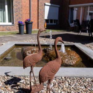 Zwei dekorative Metallflamingos stehen am Ufer eines Brunnens mit sprudelndem Wasser im Hinterhof.  | © Name