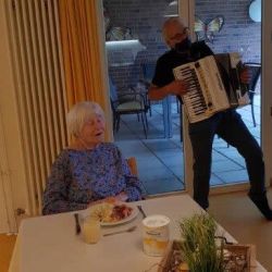Eine Frau genießt ihr Essen, während im Hintergrund ein Mann auf einem Akkordeon fröhliche Musik spielt.