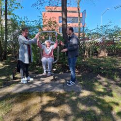 Drei Personen genießen einen sonnigen Tag im Park, während eine Frau an einer Schaukel sitzt. | © Name