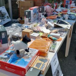 Ein Flohmarktstand vor einem Backsteingebäude bietet Plüschtiere und Brettspiele auf einem Tisch zum Verkauf an.