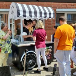 Menschen stehen vor einem Eiswagen mit gestreiftem Dach und eine Frau genießt genüsslich ihr Eis.