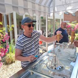 Ein Mann mit Sonnenbrille gibt ein Eis in einer Waffel an einen Kunden an einem sonnigen Tag.