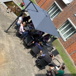 Menschen genießen ein gemütliches Treffen im Freien auf einer gepflasterten Terrasse unter großen Sonnenschirmen.