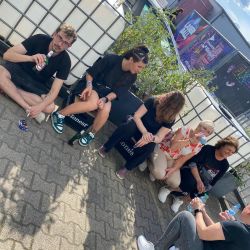 Eine Gruppe von Menschen sitzt bei strahlendem Sonnenschein auf Getränkekisten und genießt erfrischende Getränke im Freien.