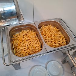Zwei große Behälter voller knuspriger Pommes frites stehen auf einem Buffet-Tisch bereit zum Servieren.