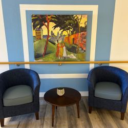 Zwei blaue Sessel flankieren einen runden Tisch vor einer lebhaften Wandkunst in einem gemütlichen Raum.