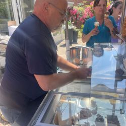 Ein Mann serviert Eis an einem Stand, während Kunden mit Eis in der Hand auf ihn warten. | © Name