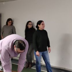 Ein Mann wählt eine Bowlingkugel aus, während drei Personen gespannt in der Kegelbahn zuschauen.