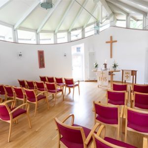 Ein heller Raum mit roten Stühlen und einem Altar mit Kreuz lädt zur Besinnung und Ruhe ein.