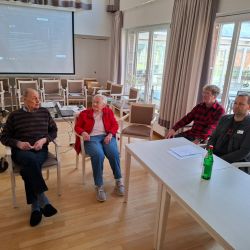 Vier Senioren sitzen in einem hellen Raum, während sie an einem Treffen teilnehmen. | © Name