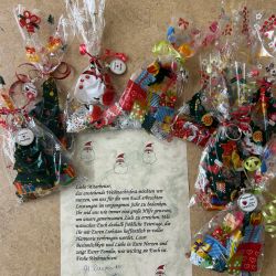 Weihnachtliche Geschenktüten und ein festlicher Brief liegen dekorativ auf einem Holztisch arrangiert.