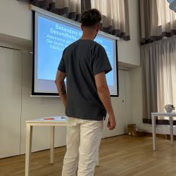 Ein Mann steht vor einer Leinwand und präsentiert Gesundheitsrisiken in einem hell erleuchteten Raum.