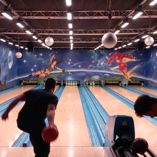 Ein Mann wirft eine rote Bowlingkugel auf einer bunt gestalteten Bahn in einer Bowlinghalle mit leuchtendem Dekor.