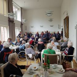Ältere Menschen genießen geselliges Beisammensein in einem hellen Raum, während eine Gruppe im Hintergrund Musik spielt.