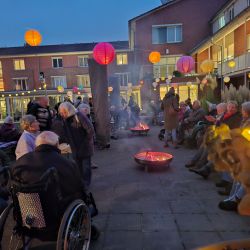 Menschen sitzen bei Dämmerung um Feuerstellen, umgeben von bunten Laternen, und genießen eine gemütliche Abendveranstaltung.
