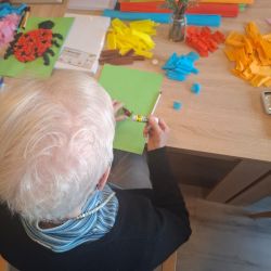 Eine Person arbeitet kreativ mit buntem Papier und Bastelmaterialien an einem Tisch.