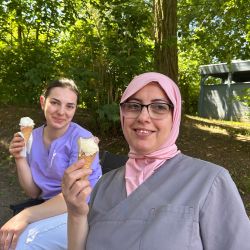 Zwei Frauen genießen an einem sonnigen Tag Eiscreme im Freien, umgeben von Bäumen und einer grünen Atmosphäre.