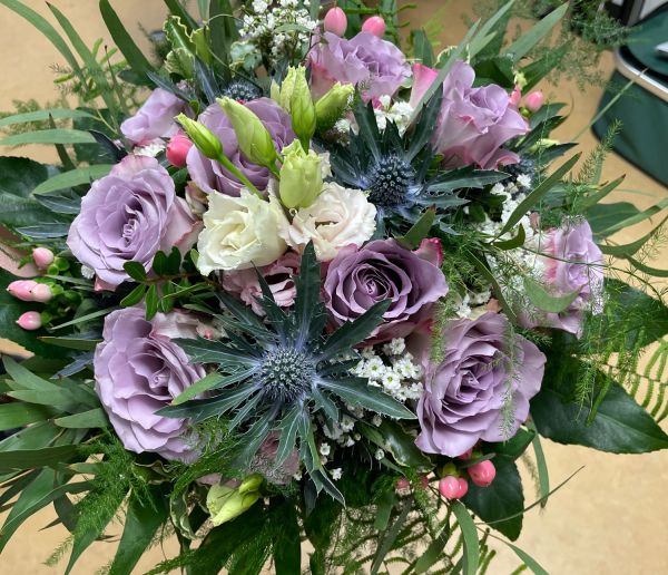 Ein üppiger Blumenstrauß mit lila Rosen und weißen Blüten entfaltet sich prächtig in voller Pracht.