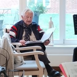 Ein älterer Mann liest entspannt ein Dokument in einem hellen Raum, während er in einem gemütlichen Sessel sitzt.