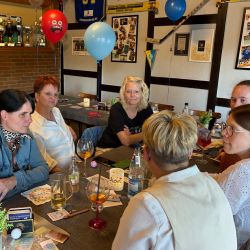 Sechs Frauen sitzen an einem Tisch, genießen Getränke und unterhalten sich in einer gemütlichen Atmosphäre.