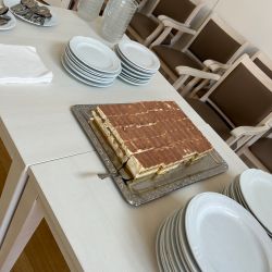 Ein Tisch mit gestapelten Tellern und einem großen Tiramisu auf einem Serviertablett lädt Gäste zum Genießen ein.